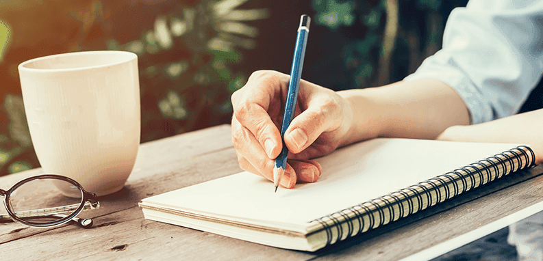 Rodzinne oszczędzanie – kobieca dłoń zapisująca ołówkiem wydatki 